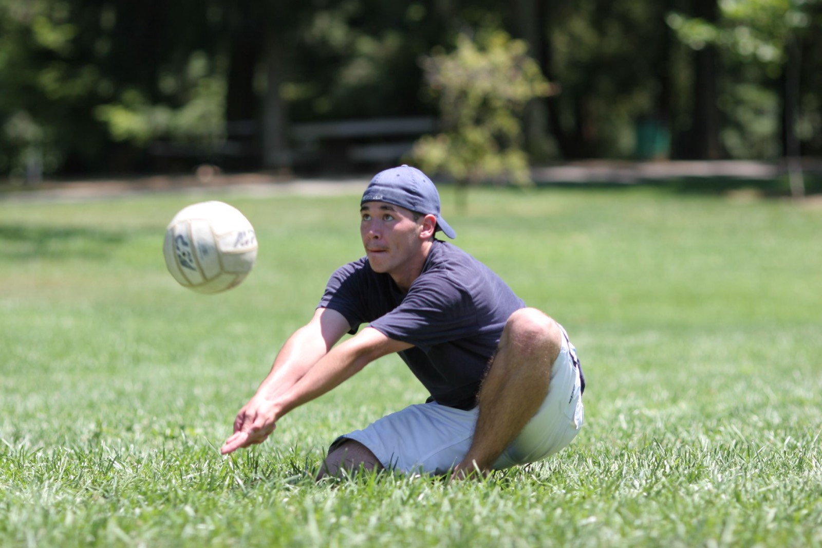 A sitting volleyball player reaching for the ball on grass in a park