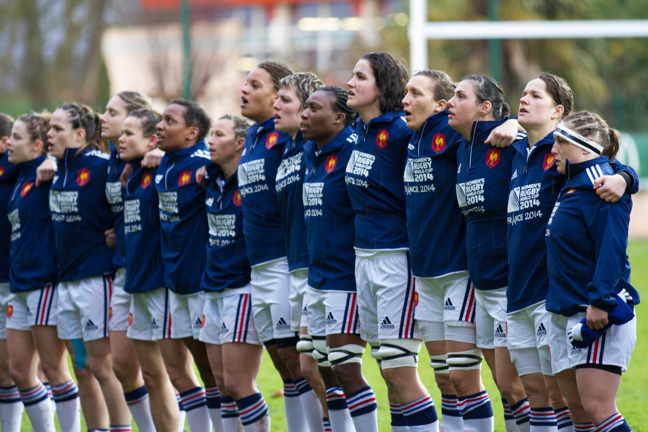 A women’s rugby side lined up arm in arm across the pitch before kick-off